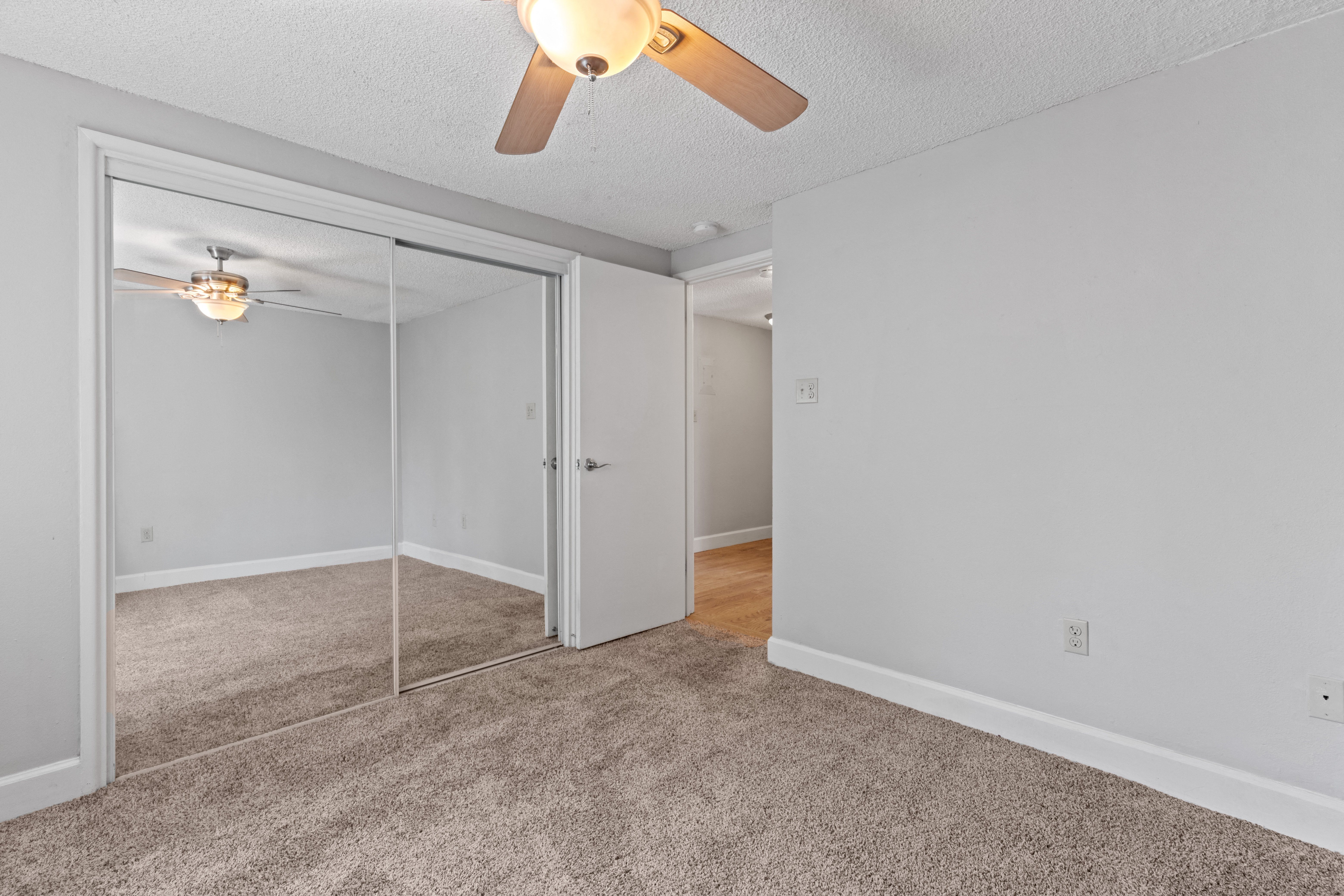 an empty bedroom with a ceiling fan and mirrored closet